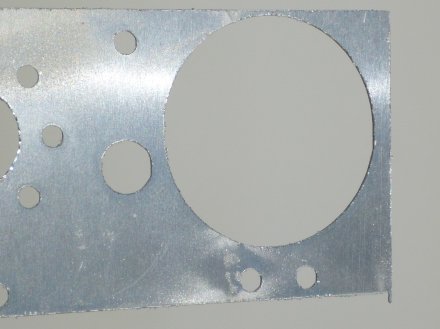 The bottom face of a part waterjet cut from soft aluminum. Note the burrs around the cut lines.